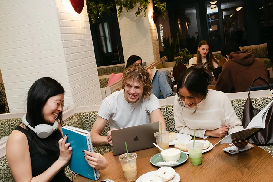 a group of young adults are studying at a booth with food and drinks