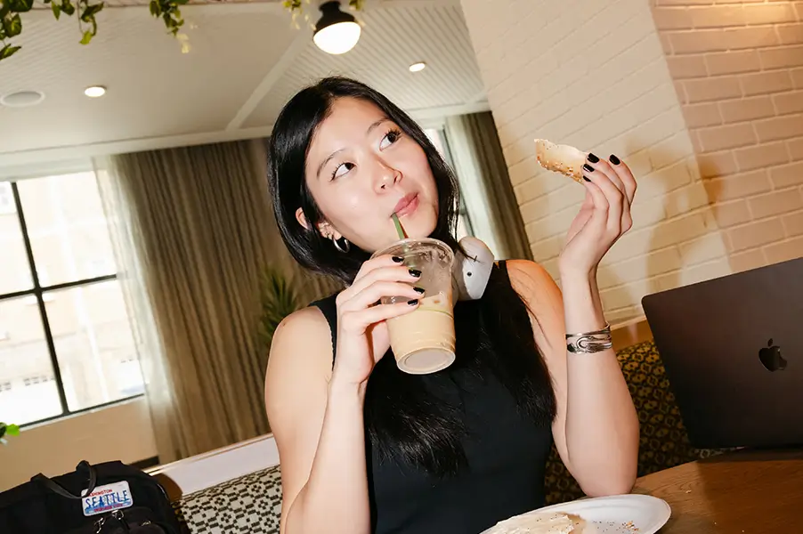a woman sipping a drink while eating a bagel