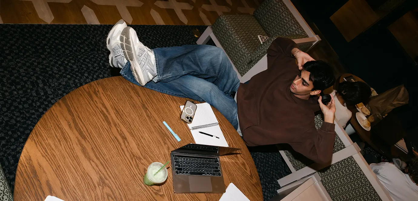 A young man sitting with a notebook and a laptop