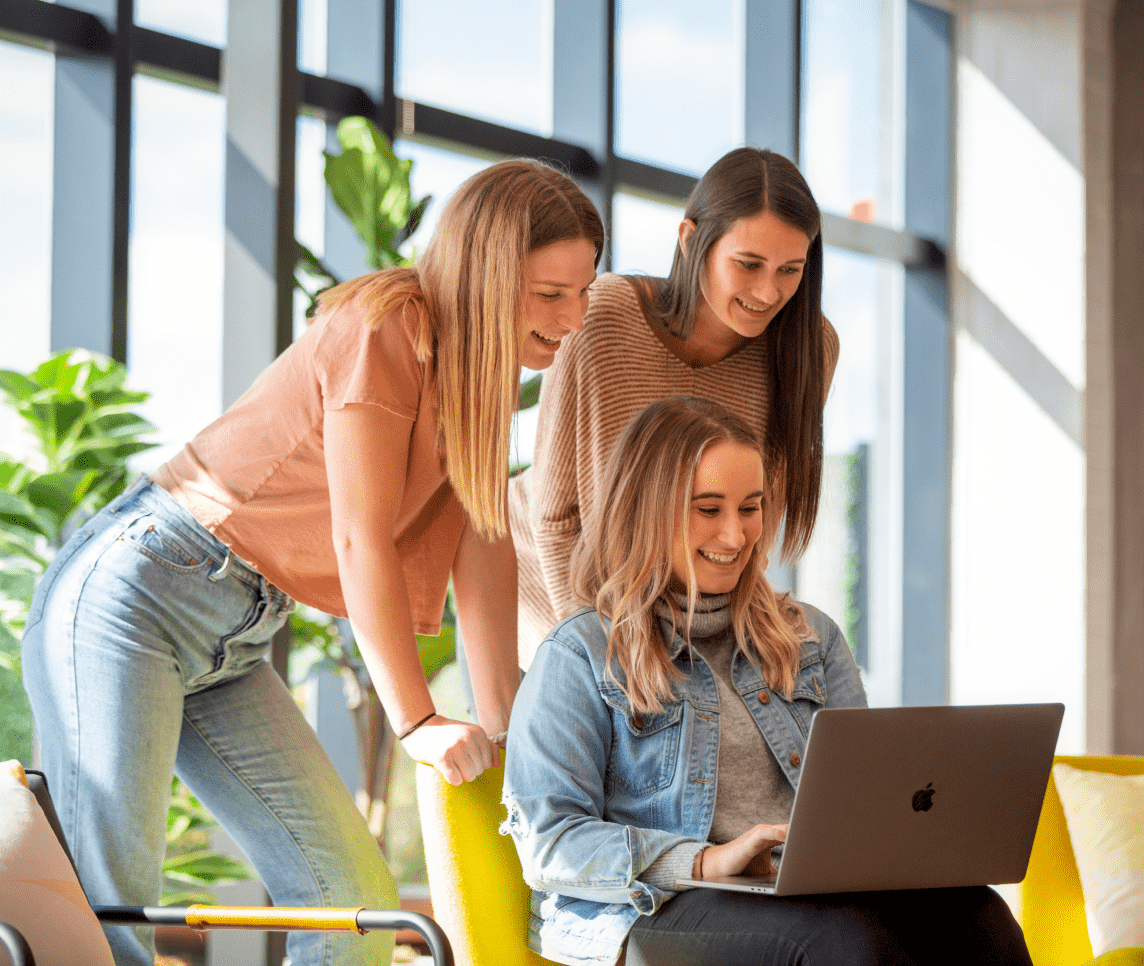 Three women smiling and looking at a laptop